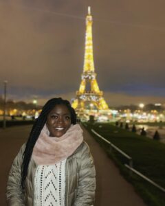 Leah stands in front of the Eiffel Tower at night.