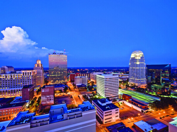This image is an aerial shot of downtown Winston-Salem at twilight. The sky is blue and the buildings are lit up by a soft orange glow.