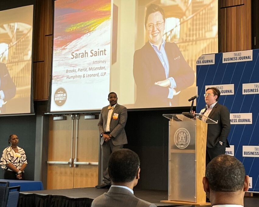 Sarah is pictured at a podium in an auditorium with her photo displayed on the projector.
