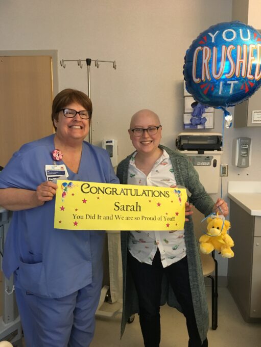 Sarah is pictured in the hospital. A nurse holds a sign that says, "Congratulations, Sarah!"