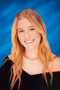 Emily Almond, a white young woman with blond hair, wears a black dress and strand of pearls.