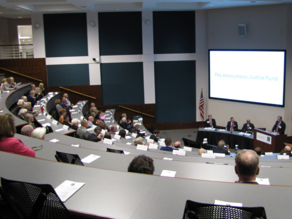 The NCBA bar center auditorium is pictured with more than 30 people sitting. Woody stands at the podium.