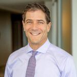 Steve, a white man with brown hair, wears a pale blue shirt and silver tie. 
