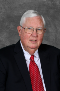 Doughton, a white man with white hair and glasses, wears a white shirt, red tie and black jacket.
