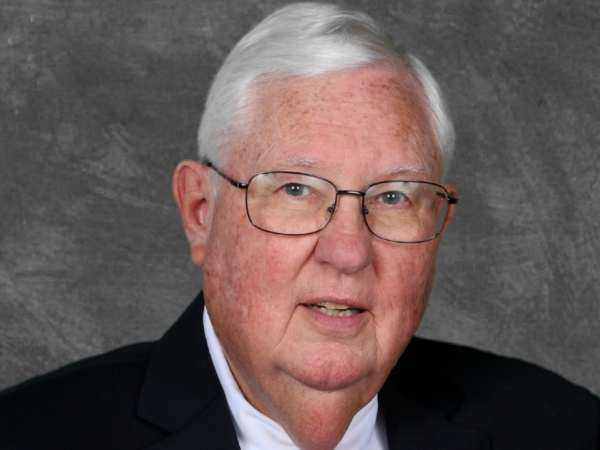 Doughton, a white man with white hair and glasses, wears a white shirt, red tie and black jacket.