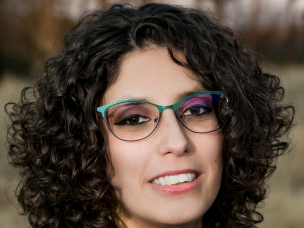 Gadalla is a woman with curly brown hair and teal glasses.