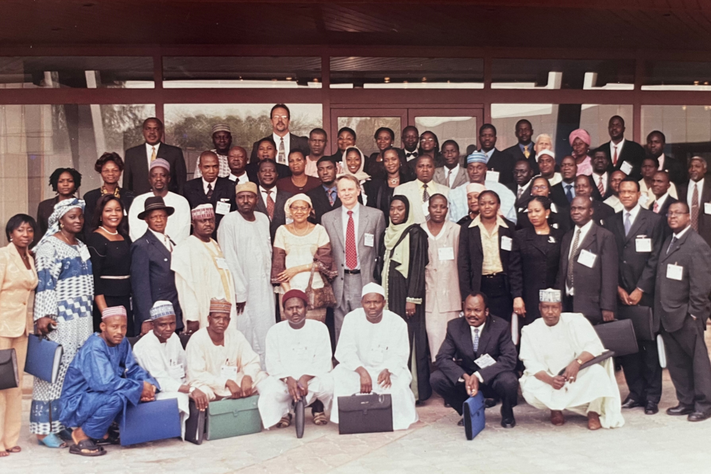 Leonard, wearing a grey suit and red tie, stands in the center of a photo with many African court administrators standing near around him.