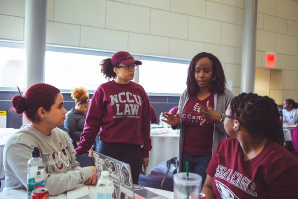 Diane Littljohn, a Black woman with black hair, wears a burgundy NCCU Law shirt and grey sweater and talks with three law students.