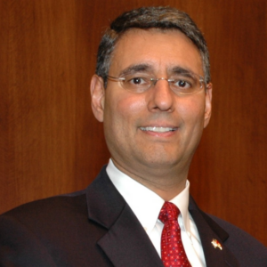 Judge Diaz, a man with brown hair and glasses, wears a white shirt, red tie, and black suit.