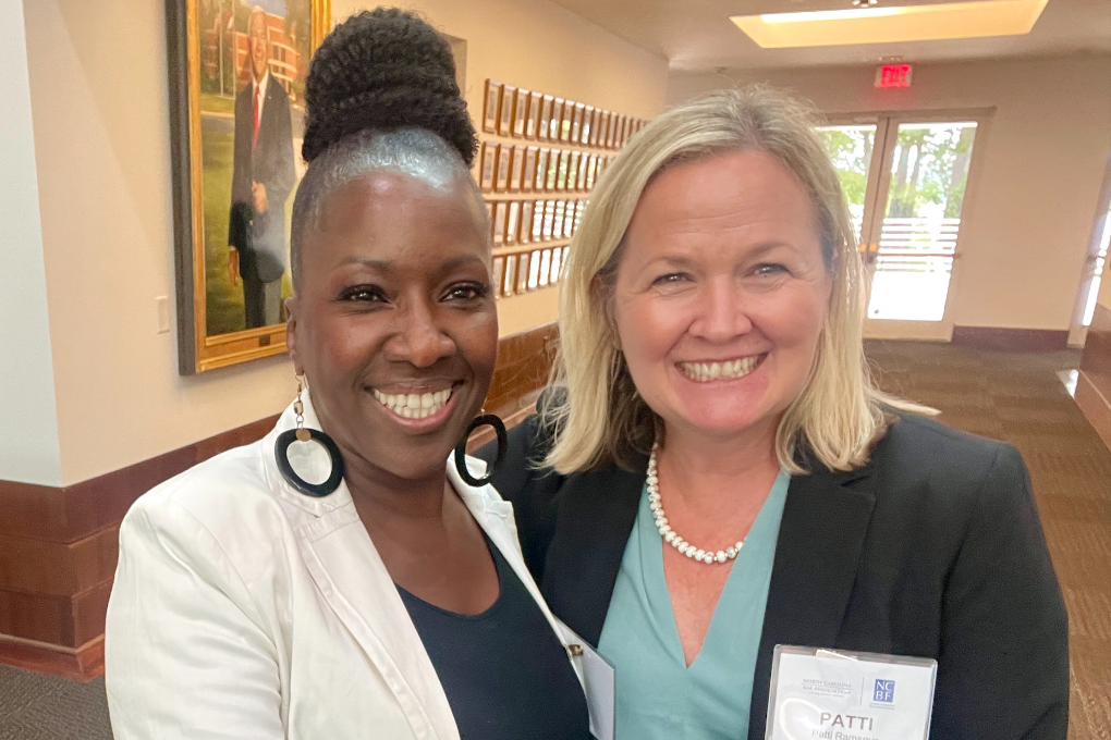 Lakisha, a Black woman with black hair, wears a black blouse and ivory jacket. She stands beside NCBA President Patti Ramseur, a white woman with blond hair, who wears a sea green blouse and black suit. They stand in the Bar Center. 