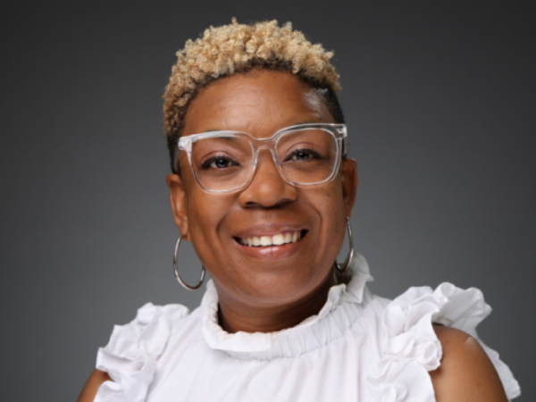 Ebony Freeland Bryant, a Black woman with short blond hair, wears clear glasses and a white sleeveless shirt with ruffles.