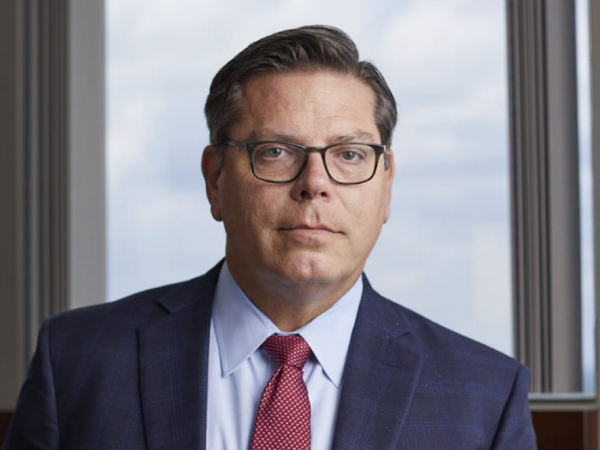 Richard Paschal, a white man with brown hair and brown glasses, wears a pale blue shirt, red tie, and navy suit.