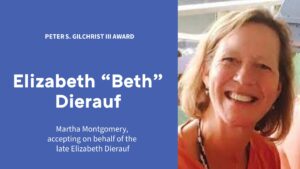 A photo of Elizabeth Dierauf is shown on a slide. In the photo, she has blond hair and an orange blouse and is pictured smiling. The slide reads "Peter S. Gilchrist III Award" and "Martha Montgomery, accepting on behalf of the late Elizabeth Dierauf."
