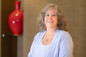 Jean, a white woman with light brown hair, wears a lavender blouse and sweater.