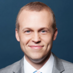 David, a white man with light brown hair, wears a white shirt and grey blazer.