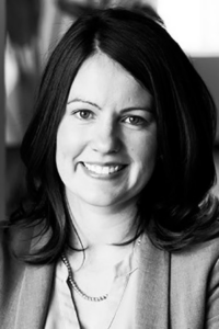 Mary, a white woman with black hair, wears a pale blouse and light jacket. She is photographed in black and white.