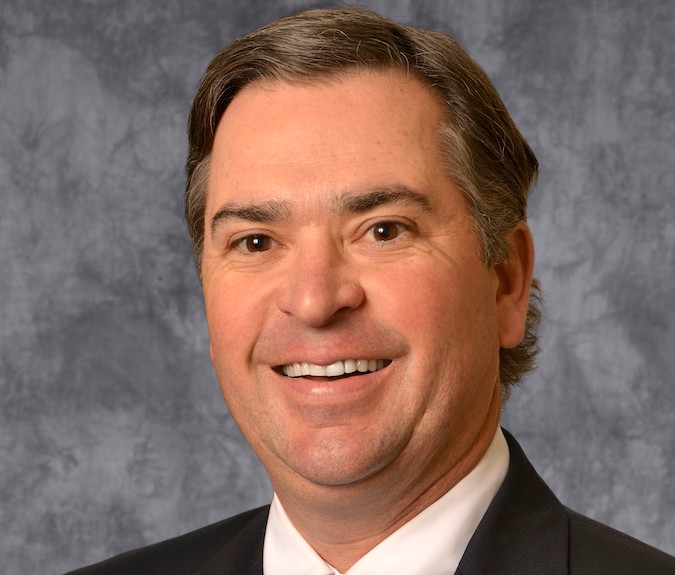 B. Ford Robertson is a white man with brown hair. He wears a white shirt and black suit.