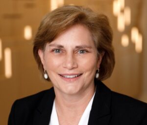 B. Joan Davis is a white woman with brown hair. She wears a white blouse and black blazer.