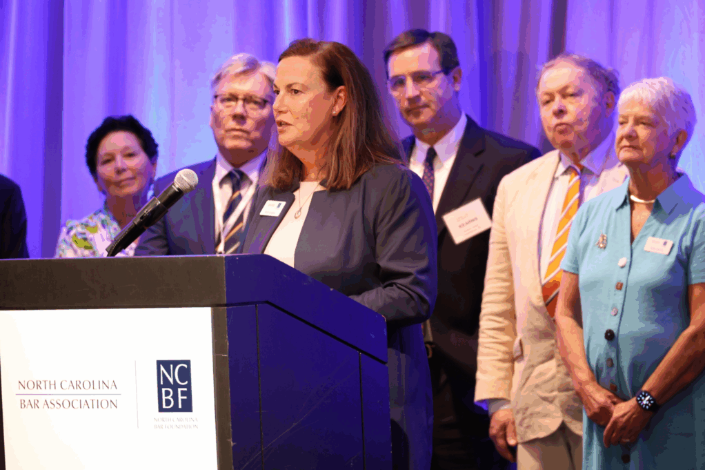 Langley, a white woman with brown hair, wears a white blouse and black suit.