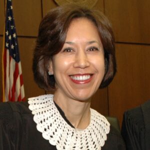 Duncan a woman with brown hair, wears a judge's robe and is pictured with the American flag behind her.