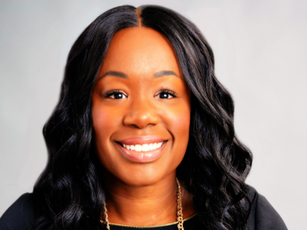 Robinson, a Black woman with black hair, wears a black blouse and sweater and a gold necklace with white and peach rhinestones.