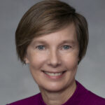 Rachel, a white woman with brown hair, wears a magenta blouse.
