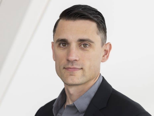 Bowyer, a white man with brown hair, wears a grey shirt and a black suit.