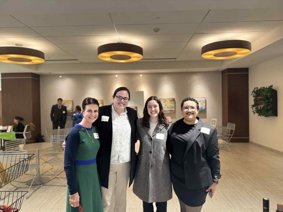 Risser wears a black dress and black blazer. Jennifer, a white woman with brown hair, wears a green dress. Taylor, a white woman with brown hair, wears a white shirt and black blazer, and Lauren, a white woman with brown hair wears a white blouse and grey jacket.