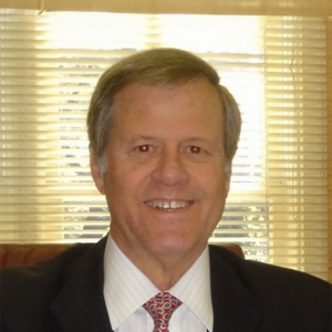 Robert Baker, a white man with grey hair, wears a white shirt, red tie and black jacket.