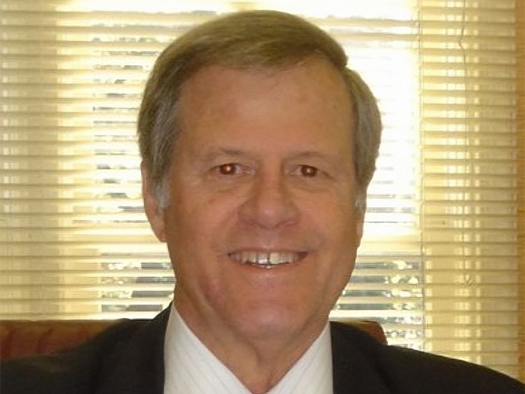 Robert Baker, a white man with grey hair, wears a white shirt, red tie and black jacket.