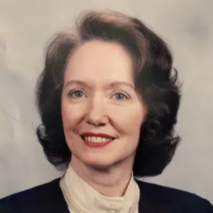 Rhoda, a white woman with brown hair, wears a white blouse and black jacket.