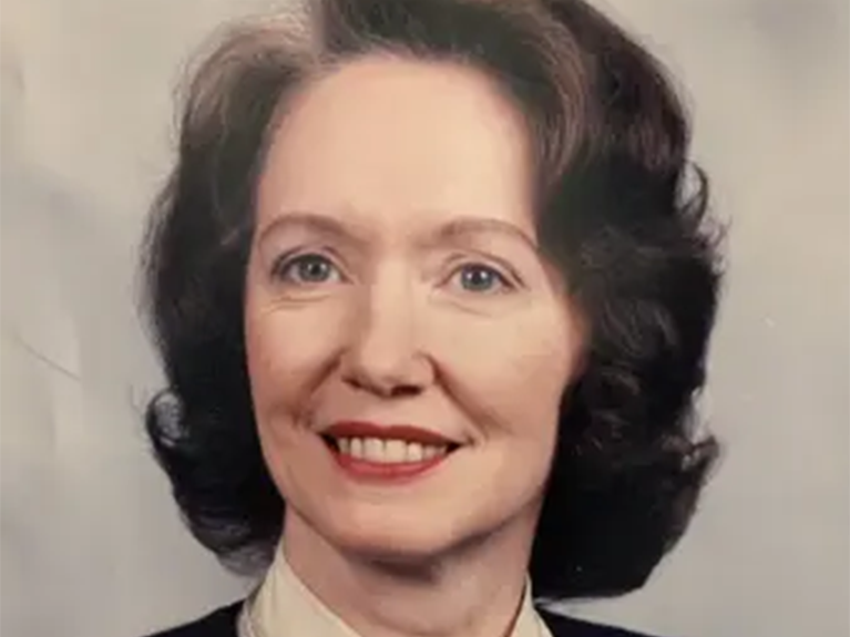 Rhoda, a white woman with brown hair, wears a white blouse and black jacket.