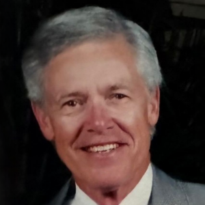 Robert, a white man with grey hair, wears a white shirt and grey suit.