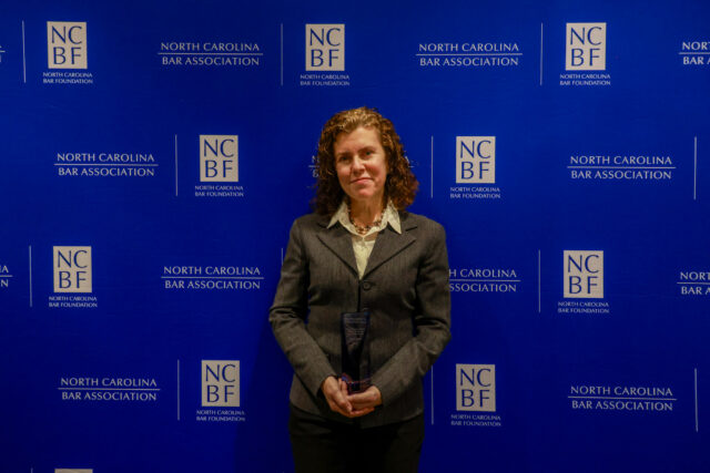 Connie, a white woman with curly brown hair, wears a white blouse and grey blazer.