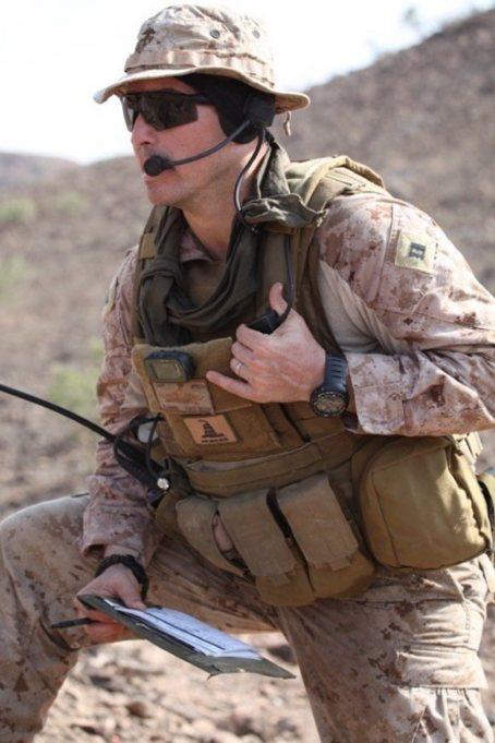 Plummer is wearing his military uniform, which has a camoflage pattern. He is speaking into his speaker microphone.