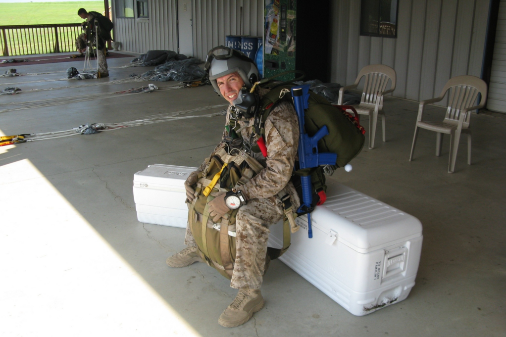 Plummer, wearing his military uniform and gear for the training jump, rests on a white ice chest and is smiling.