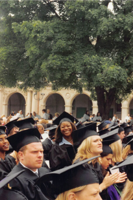 Micah is looking at the camera in a group of law school graduates. She is photographed in her doctoral regalia and is smiling. 