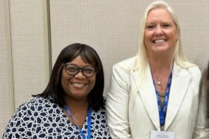 Micah, a Black woman with black hair, wears a white and black shirt and black glasses. Janice, a white woman with blond hair, wears a blue shirt and white blazer.